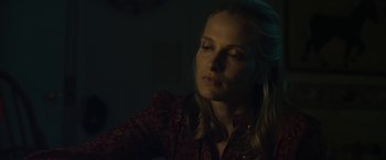 Movie still from “Cold in July” (2014), directed by Jim Mickle – A woman in a red shirt is sitting in a dark room; Close Up shot, Over the shoulder angle