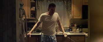 Movie still from “Cold in July” (2014), directed by Jim Mickle – A man holding a phone in his hands in a kitchen; Medium shot, Low angle