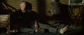 Movie still from “Cold in July” (2014), directed by Jim Mickle – A man sitting on the ground in front of an old fashioned stove; Medium shot, High angle