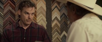 Movie still from “Cold in July” (2014), directed by Jim Mickle – A man standing in front of a wall of picture frames; Close Up shot, Over the shoulder angle