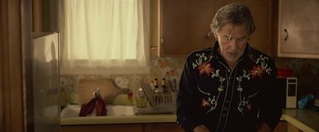 Movie still from “Cold in July” (2014), directed by Jim Mickle – An older woman standing in a kitchen next to a sink; Medium shot, Over the shoulder angle