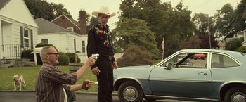 Movie still from “Cold in July” (2014), directed by Jim Mickle – A man wearing a cowboy hat standing in front of a car; Medium shot, Over the shoulder angle