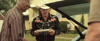 Movie still from “Cold in July” (2014), directed by Jim Mickle – A man wearing a cowboy hat holding an electronic device; Medium shot, Over the shoulder angle