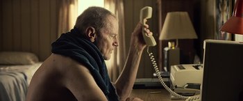 Movie still from “Cold in July” (2014), directed by Jim Mickle – An older man is holding a phone up to his ear; Medium shot, Low angle