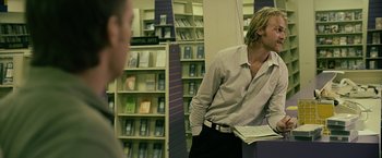 Movie still from “Cold in July” (2014), directed by Jim Mickle – A man standing in front of a bookcase holding papers; Medium shot, Over the shoulder angle