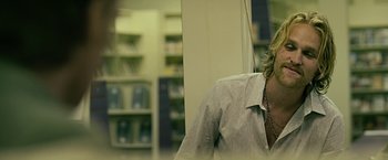 Movie still from “Cold in July” (2014), directed by Jim Mickle – A man wearing a white dress shirt is standing in front of a book shelf; Close Up shot, Over the shoulder angle