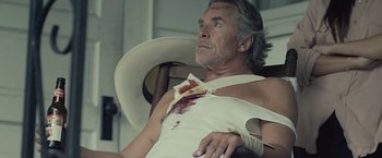 Movie still from “Cold in July” (2014), directed by Jim Mickle – An old man with a bandage on his arm and a bandage on his chest; Medium shot, Low angle