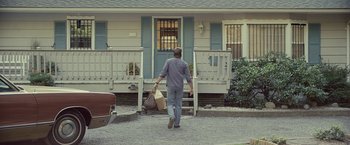 Movie still from “Cold in July” (2014), directed by Jim Mickle – A man walking down the street with a bag of groceries; Wide shot, Over the shoulder angle