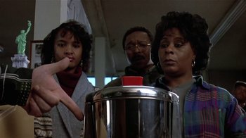 Movie still from “Coneheads” (1993), directed by Steve Barron – A group of people standing next to each other in front of a coffee pot; Close Up shot, Low angle