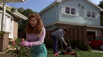 Movie still from “Coneheads” (1993), directed by Steve Barron – A woman standing next to a man in a yard; Medium shot, Low angle