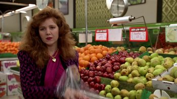 Movie still from “Coneheads” (1993), directed by Steve Barron – A woman standing in front of a display of fruit; Medium shot, Over the shoulder angle