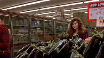 Movie still from “Coneheads” (1993), directed by Steve Barron – A woman standing in front of a pile of eggplant in a grocery store; Medium shot, Low angle
