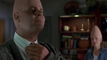 Movie still from “Coneheads” (1993), directed by Steve Barron – A bald man in a suit and tie holding a sweater over his neck; Close Up shot, Low angle