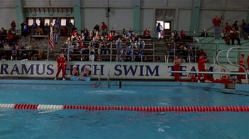 Movie still from “Coneheads” (1993), directed by Steve Barron – Spectators watching swimmers in the pool during a competition; Extreme Wide shot, High angle