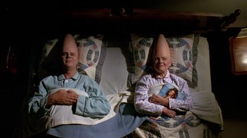 Movie still from “Coneheads” (1993), directed by Steve Barron – A couple of people that are in some kind of hats; Medium shot, High angle
