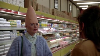 Movie still from “Coneheads” (1993), directed by Steve Barron – A person wearing a fake hat in a grocery store; Close Up shot, High angle