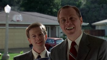 Movie still from “Coneheads” (1993), directed by Steve Barron – A couple of men standing next to each other in suits; Medium shot, Low angle