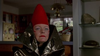 Movie still from “Coneheads” (1993), directed by Steve Barron – A woman wearing a red hat and a silver cape; Close Up shot, Low angle