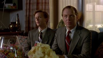 Movie still from “Coneheads” (1993), directed by Steve Barron – A couple of men in suits sitting next to each other in a room; Close Up shot, Low angle