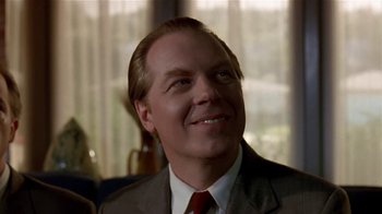 Movie still from “Coneheads” (1993), directed by Steve Barron – A man in a brown suit and red neck tie smiling; Close Up shot, Low angle