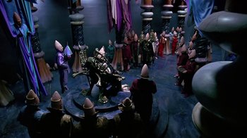 Movie still from “Coneheads” (1993), directed by Steve Barron – A group of people standing in a room with hats on their heads; Extreme Wide shot, High angle