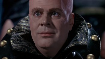 Movie still from “Coneheads” (1993), directed by Steve Barron – A bald man wearing a black and gold jacket; Close Up shot, Low angle