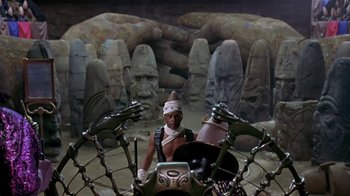 Movie still from “Coneheads” (1993), directed by Steve Barron – A man sitting on a motorcycle in front of some statues; Wide shot, High angle