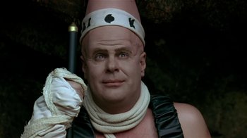 Movie still from “Coneheads” (1993), directed by Steve Barron – A bald man with a white hat is holding an umbrella; Close Up shot, High angle