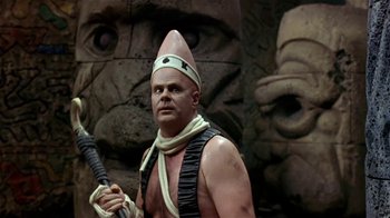 Movie still from “Coneheads” (1993), directed by Steve Barron – A man with a helmet and a sword in front of a statue of a face; Close Up shot, Low angle