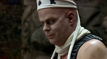 Movie still from “Coneheads” (1993), directed by Steve Barron – A bald man wearing a white hat and a black vest; Close Up shot, Low angle