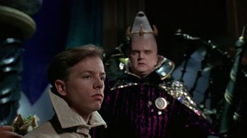 Movie still from “Coneheads” (1993), directed by Steve Barron – A man and a man in a purple and black outfit; Medium shot, Over the shoulder angle