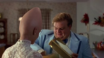 Movie still from “Coneheads” (1993), directed by Steve Barron – A bald man in a blue suit is holding an open box; Close Up shot, Over the shoulder angle