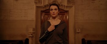 Movie still from “Constantine” (2005), directed by Francis Lawrence – A woman standing in front of a door wearing a necklace; Medium shot, Over the shoulder angle