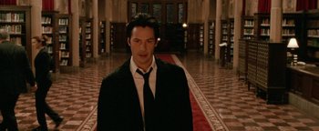Movie still from “Constantine” (2005), directed by Francis Lawrence – A man wearing a suit and tie standing in a library; Medium shot, Low angle