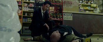 Movie still from “Constantine” (2005), directed by Francis Lawrence – A man in a suit and tie is kneeling over another man in a suit; Medium shot, Low angle