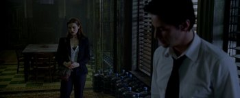 Movie still from “Constantine” (2005), directed by Francis Lawrence – A man and a woman standing next to each other in front of water bottles; Wide shot, Over the shoulder angle