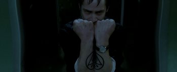 Movie still from “Constantine” (2005), directed by Francis Lawrence – A man with his hands over his face with a tattoo; Close Up shot, Overhead angle