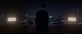 Movie still from “Constantine” (2005), directed by Francis Lawrence – A man standing in front of a window at night looking out at the city lights; Extreme Wide shot, Low angle
