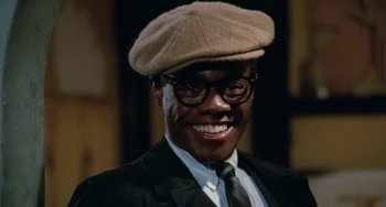 Movie still from “Cooley High” (1975), directed by Michael Schultz – A man wearing a hat and glasses smiling for the camera; Close Up shot, Low angle
