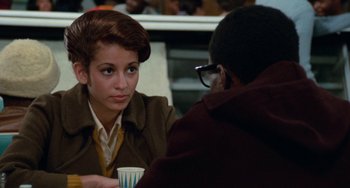 Movie still from “Cooley High” (1975), directed by Michael Schultz – A woman sitting at a table holding a cup; Medium shot, Over the shoulder angle