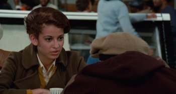 Movie still from “Cooley High” (1975), directed by Michael Schultz – A woman sitting at a table holding a cup of coffee; Medium shot, Over the shoulder angle