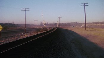 Movie still from “Coonskin” (1974), directed by Ralph Bakshi – A train track next to a road with power lines on it; Extreme Wide shot, High angle