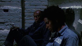 Movie still from “Coonskin” (1974), directed by Ralph Bakshi – Two men sitting next to each other on a brick wall; Medium shot, High angle