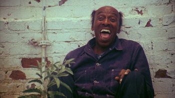 Movie still from “Coonskin” (1974), directed by Ralph Bakshi – A man sitting on the ground with his mouth wide open; Close Up shot, High angle