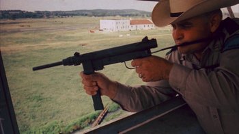 Movie still from “Coonskin” (1974), directed by Ralph Bakshi – A man holding a machine gun up to a window; Medium shot, High angle