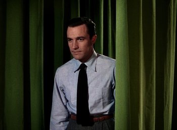 Movie still from “Cover Girl” (1944), directed by Charles Vidor – A man in a dress shirt and tie standing in front of green curtains; Medium shot, Low angle