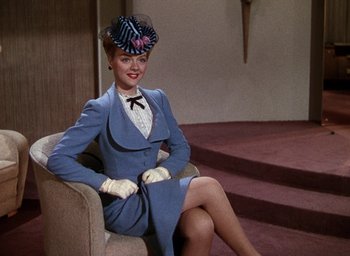 Movie still from “Cover Girl” (1944), directed by Charles Vidor – A woman sitting on top of a chair wearing a suit and hat; Medium shot, Low angle