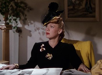 Movie still from “Cover Girl” (1944), directed by Charles Vidor – A woman sitting at a table wearing a hat; Medium shot, Low angle