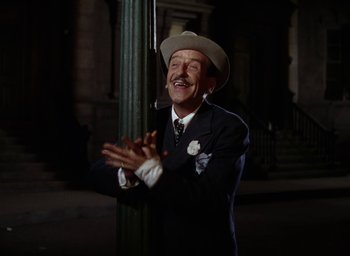 Movie still from “Cover Girl” (1944), directed by Charles Vidor – A man wearing a suit and a hat standing next to a pole; Medium shot, Low angle