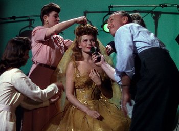 Movie still from “Cover Girl” (1944), directed by Charles Vidor – A group of people standing next to a woman in a yellow dress; Medium shot, Over the shoulder angle